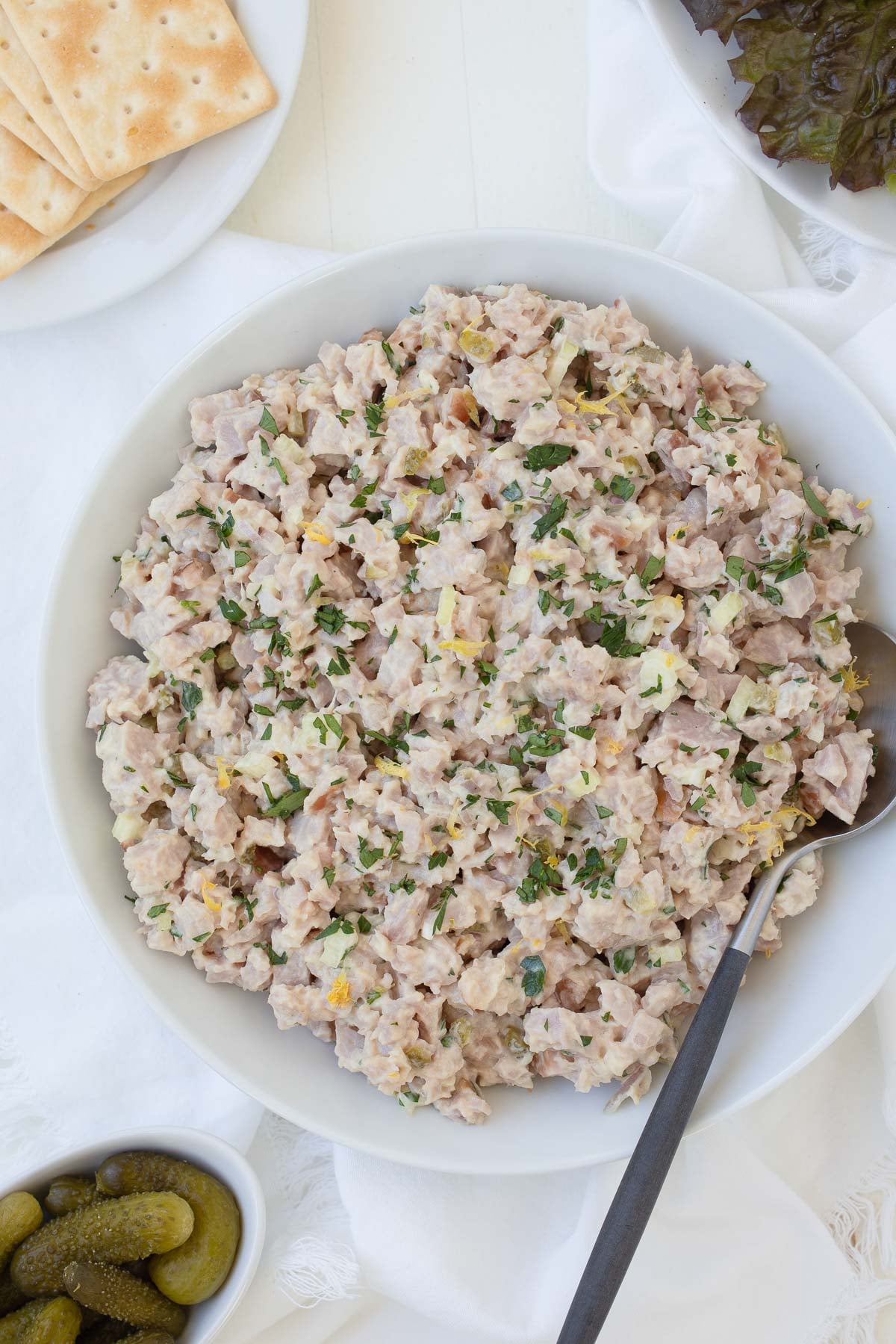 A bowl of ham salad with sprinkles of chopped parsley and lemon zest with crackers on the side.