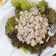 Creamy ham salad piled on red leaf lettuce greens with a fork on a white plate.