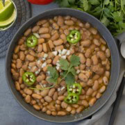 A bowl of slow cooker pinto beans topped with jalapeno slices, cilantro, and chopped white onion.