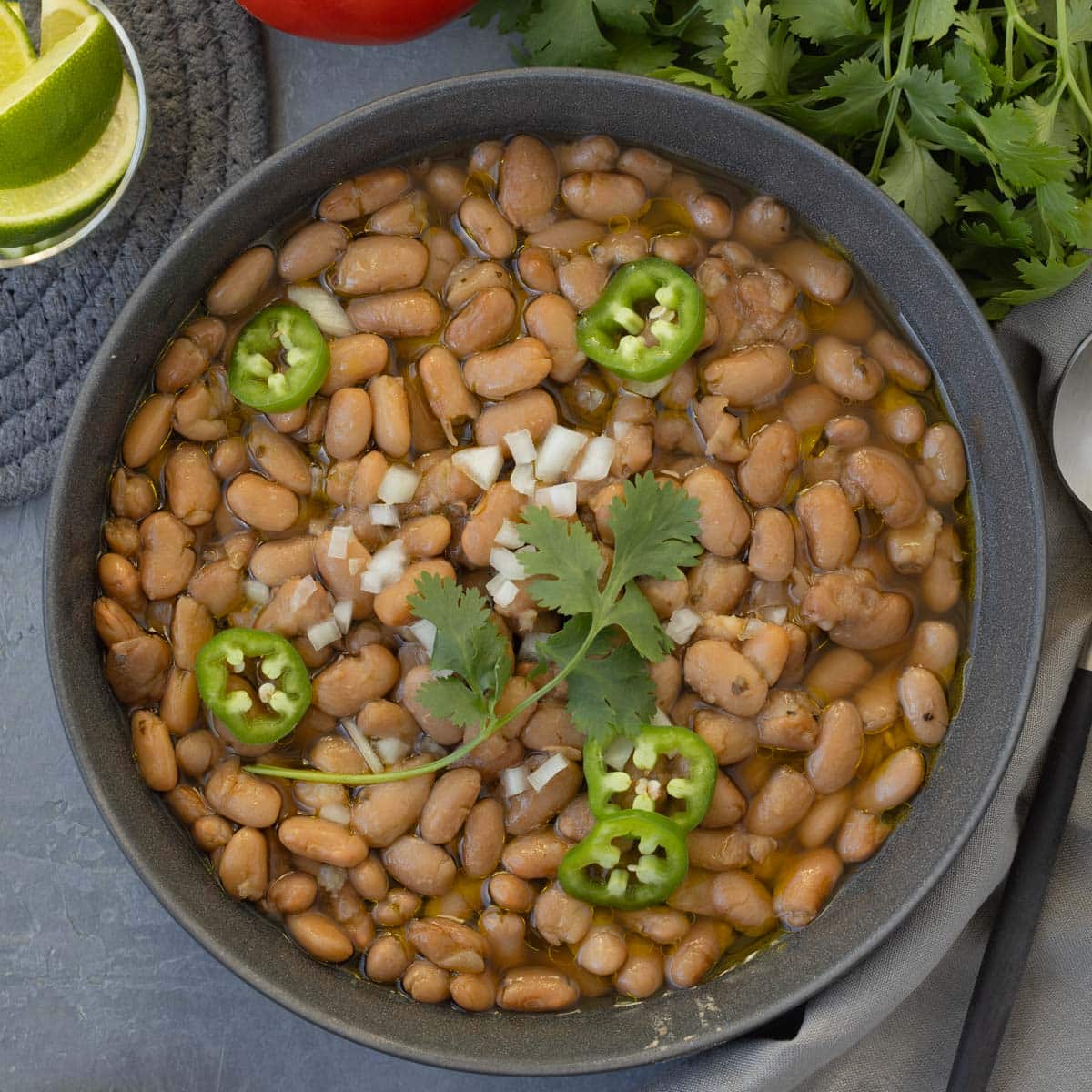 A bowl of slow cooker pinto beans topped with jalapeno slices, cilantro, and chopped white onion.