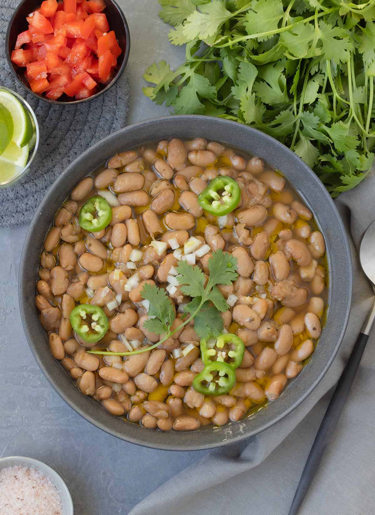 A bowl of creamy pinto beans in a gray bowl with chopped white onion, cilantro, and slices of jalapeno.