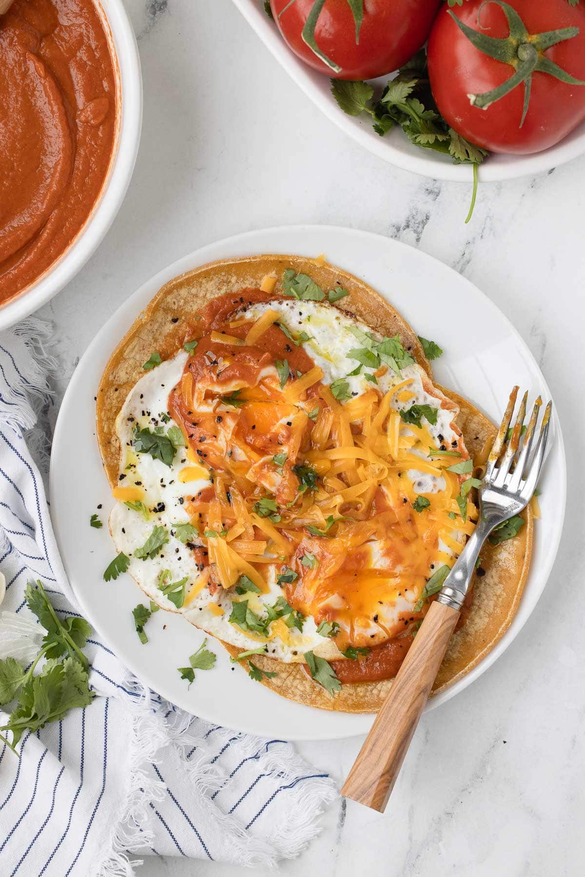 A plate of huevos rancheros, corn tortillas topped with fried eggs, cheese and ranchero sauce.