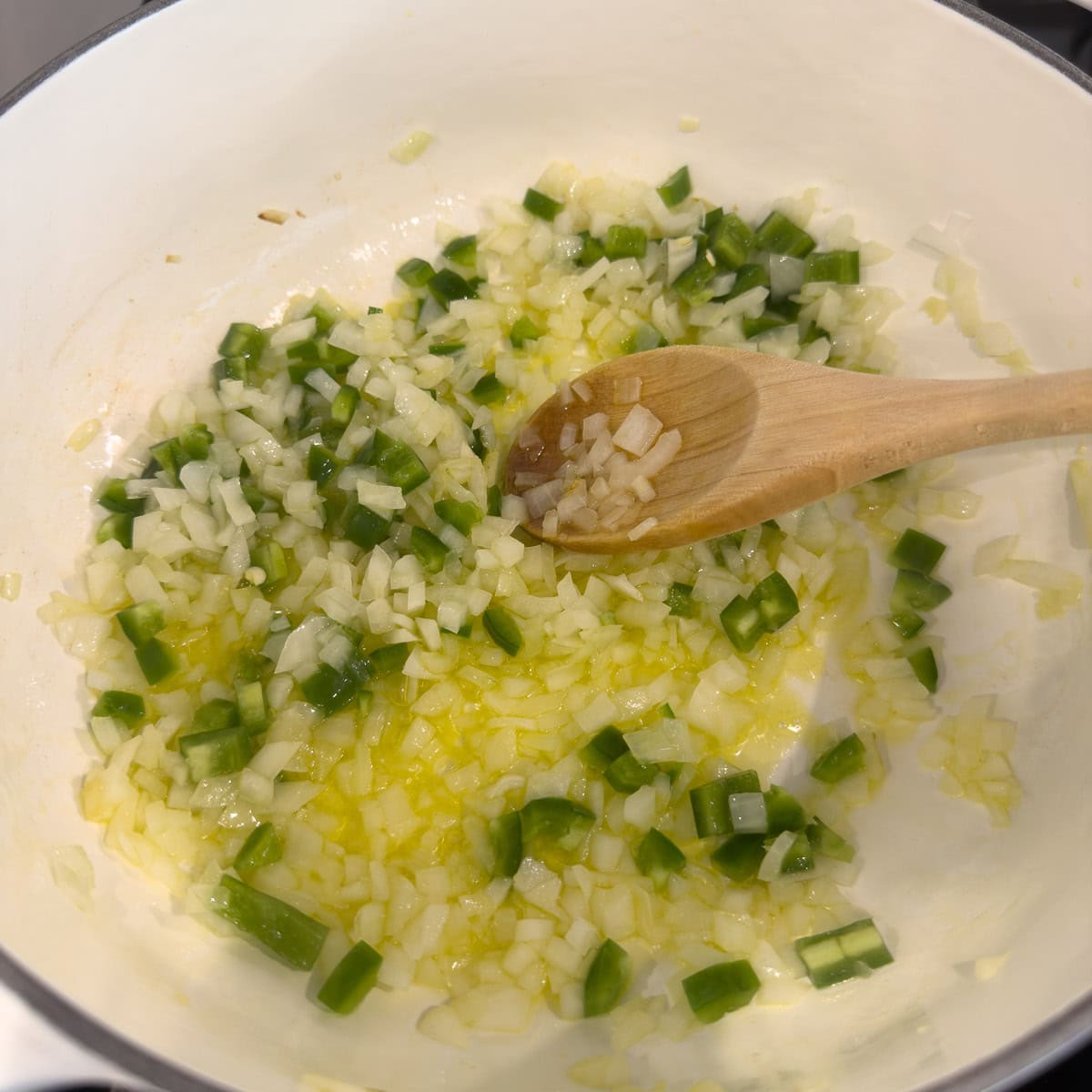 Chilies, onions, and oil cooking in olive oil in a white pot.