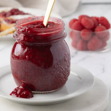 Ruby red raspberry sauce made with frozen berries in a glass jar with a gold spoon.