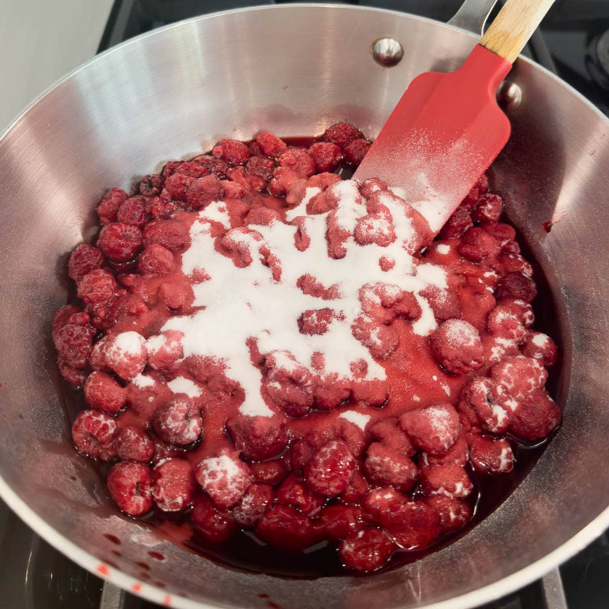 Adding sweetener to a pot of cooking raspberries for a raspberry sauce.
