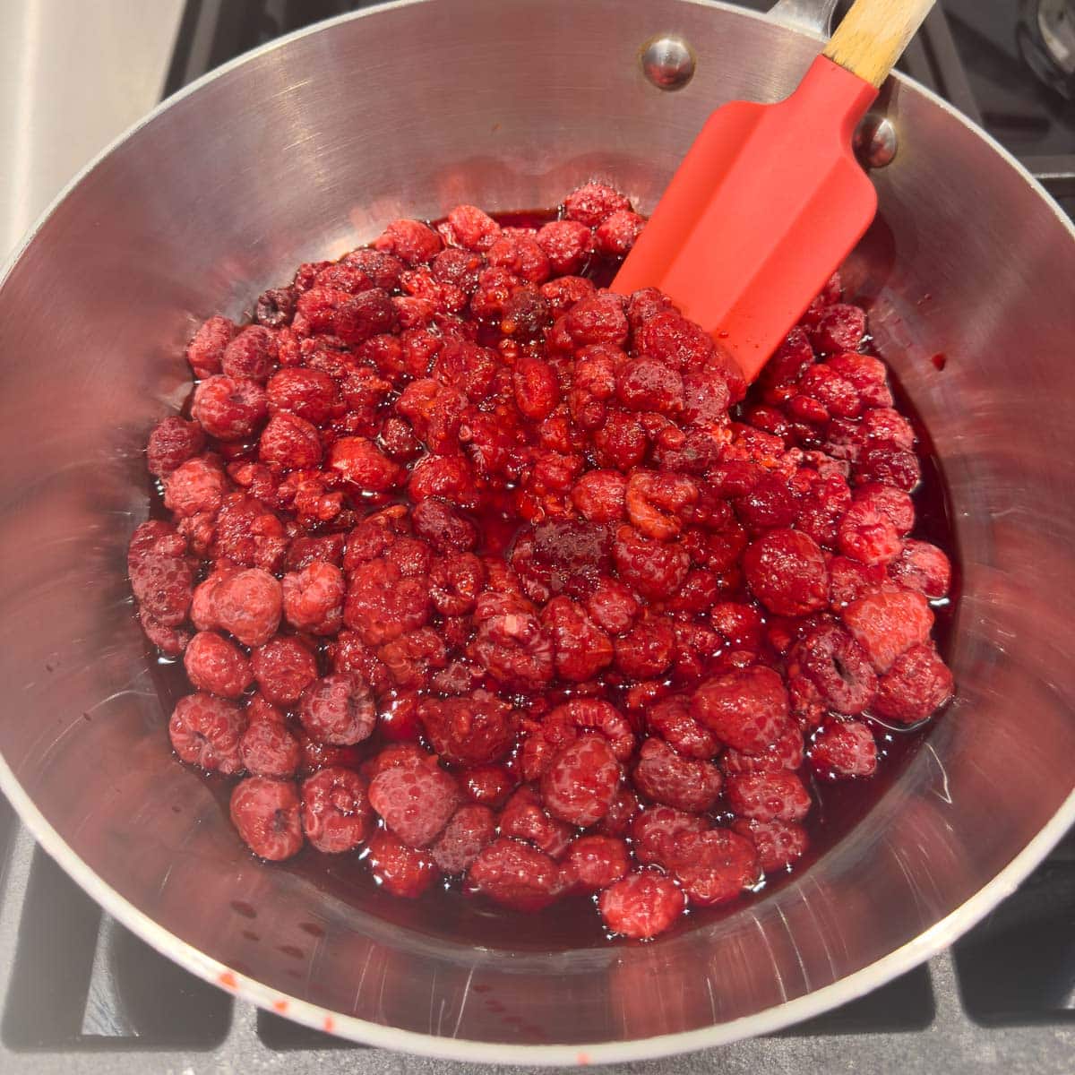 Frozen raspberries thawing and cooking in a stainless steel pot.