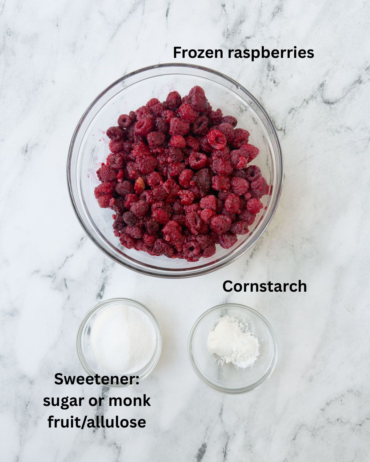 Frozen raspberries, with sugar and cornstarch in bowls on marble counter.
