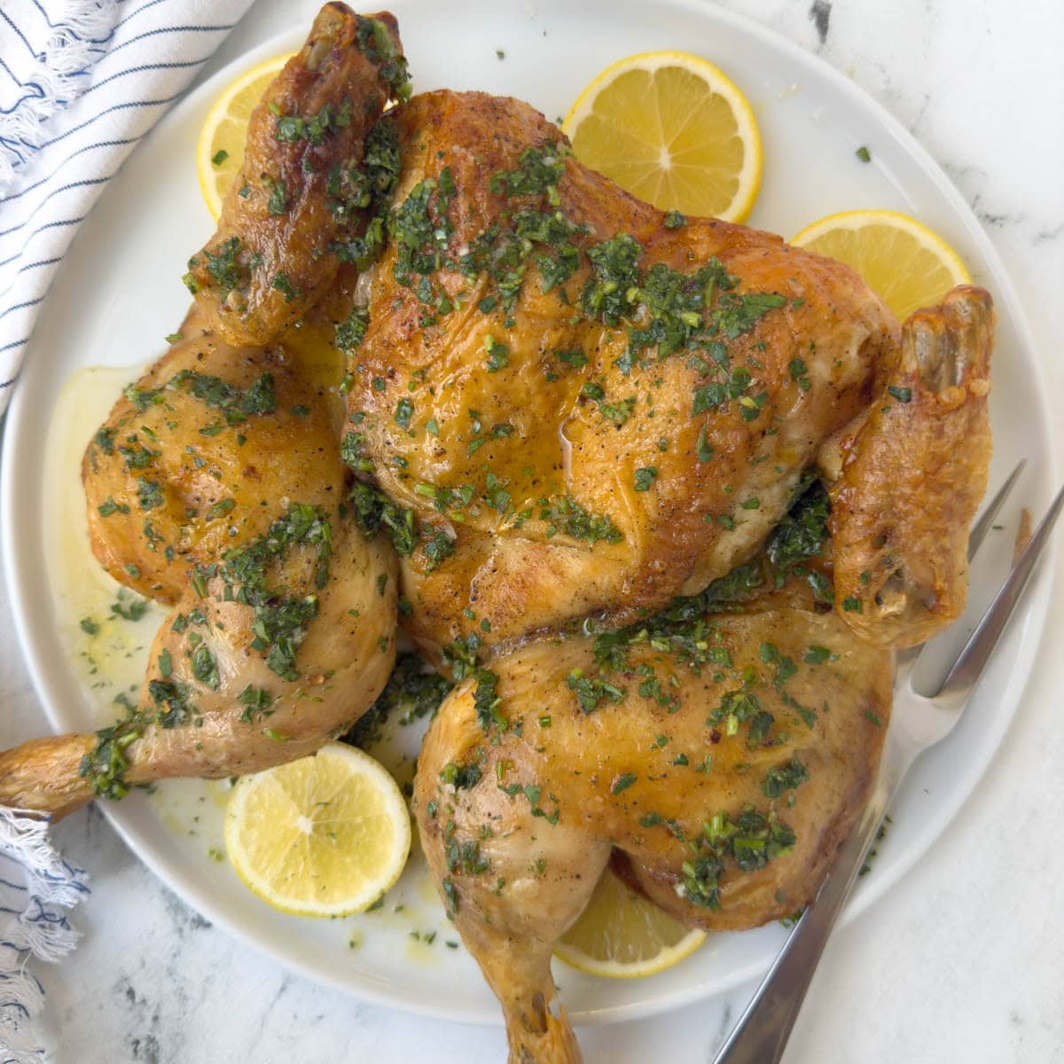 Spatchcock roasted chicken on a round serving platter drizzled with lemon herb sauce.