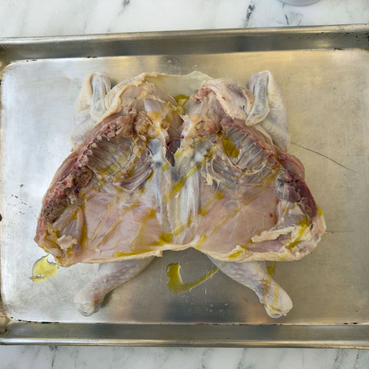 The underside of a spatchcock chicken with oil oil on a sheet tray.
