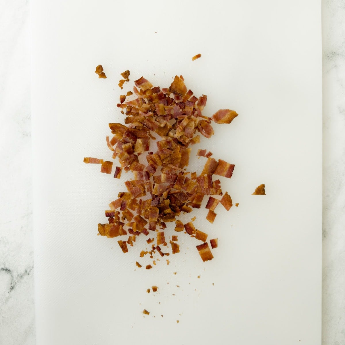 Chopped crisp bacon on a white cutting board.