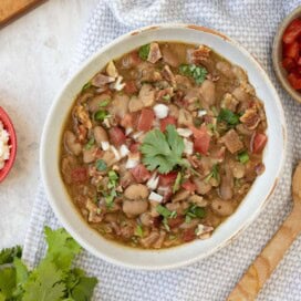 Charro beans in a rustic bowl with chopped tomatoes and sprinkles of white onion and cilantro.