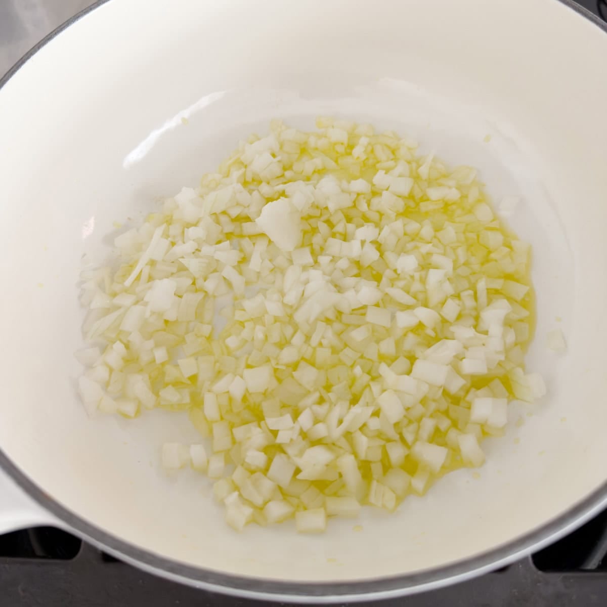 Chopped white onions sautéing in olive oil in a white pot.