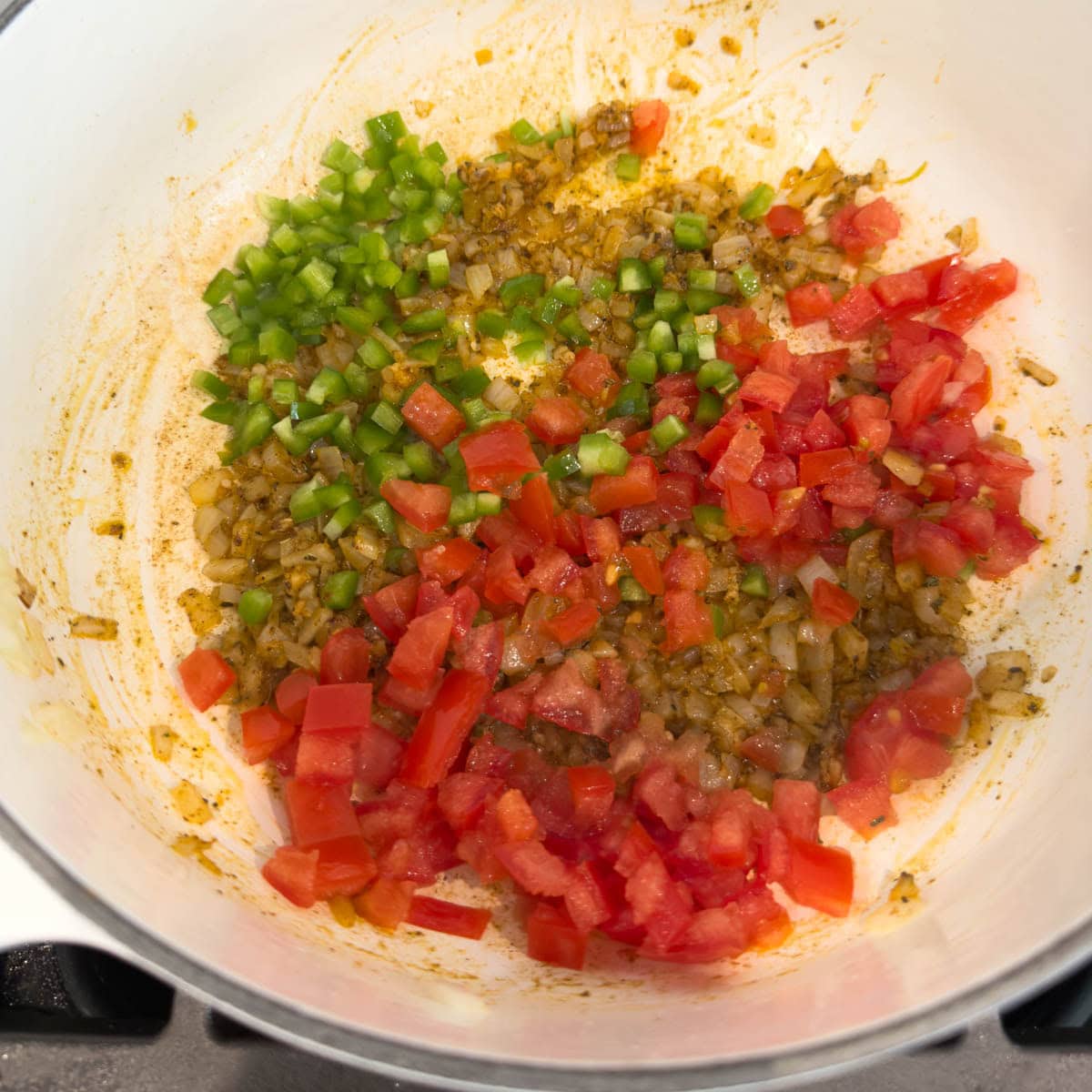 Adding chopped tomatoes and chopped jalapeno pepper to a pot of onions, herbs and spices for beans.