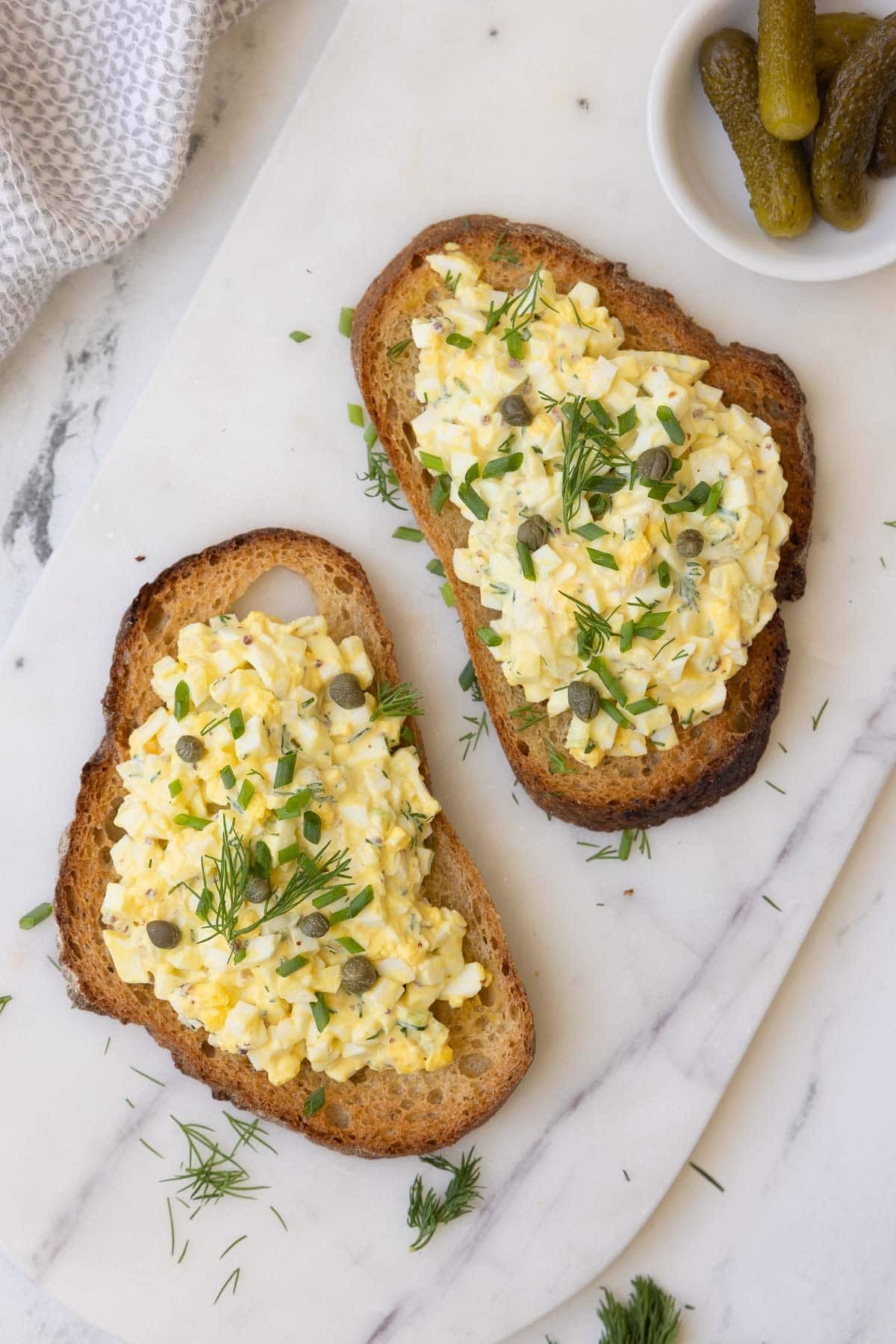 Egg salad open faced sandwiches garnished with chopped herbs and capers.