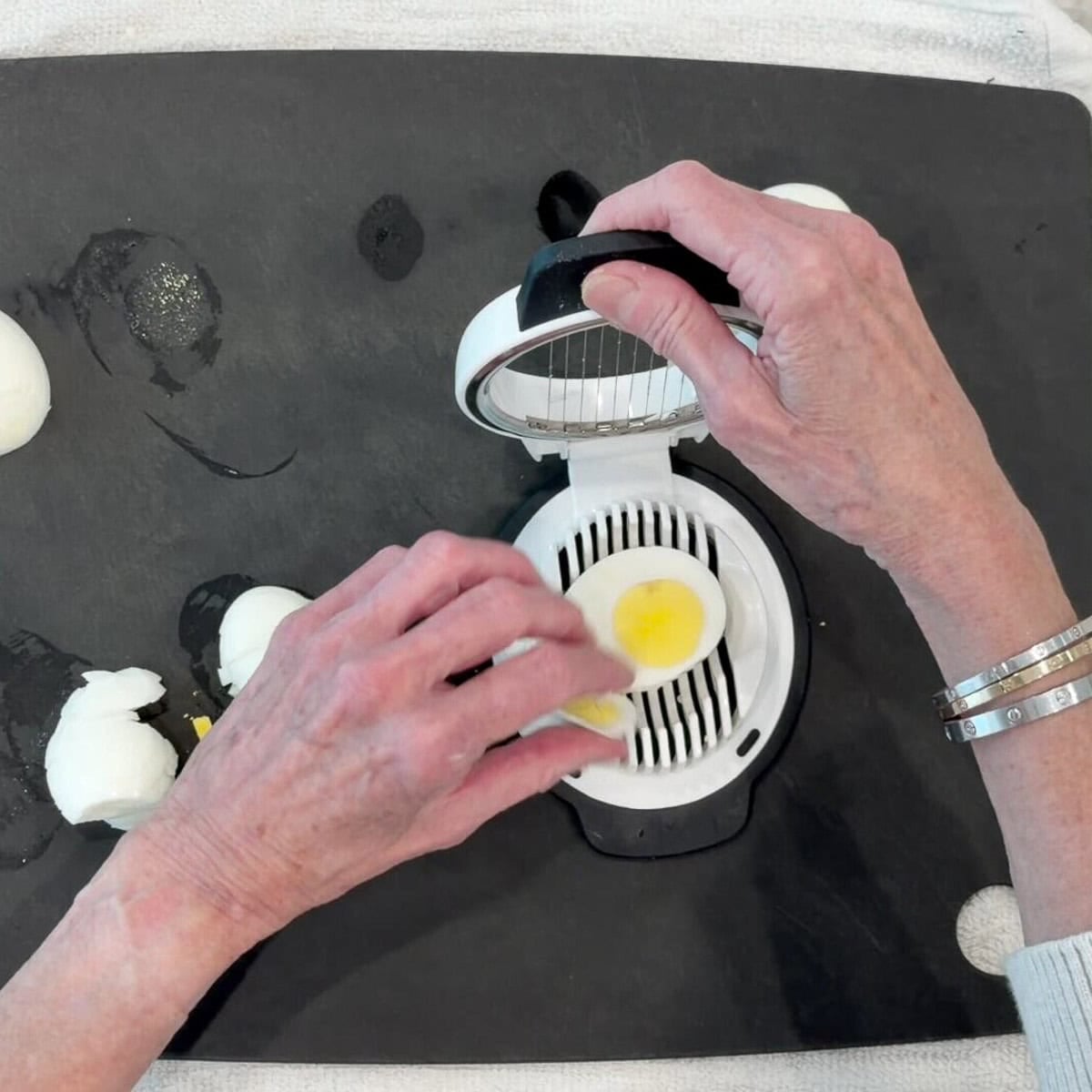 Slicing hard boiled eggs with an egg slicer on a black cutting board.