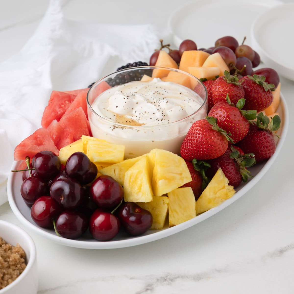 Brightly colored fresh fruit platter with a druit dip in the center drizzled with honey and vanilla bean.