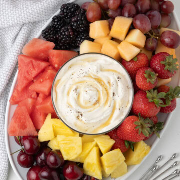 A sour cream and honey fruit dip surrounded by fresh fruit on an oval platter.