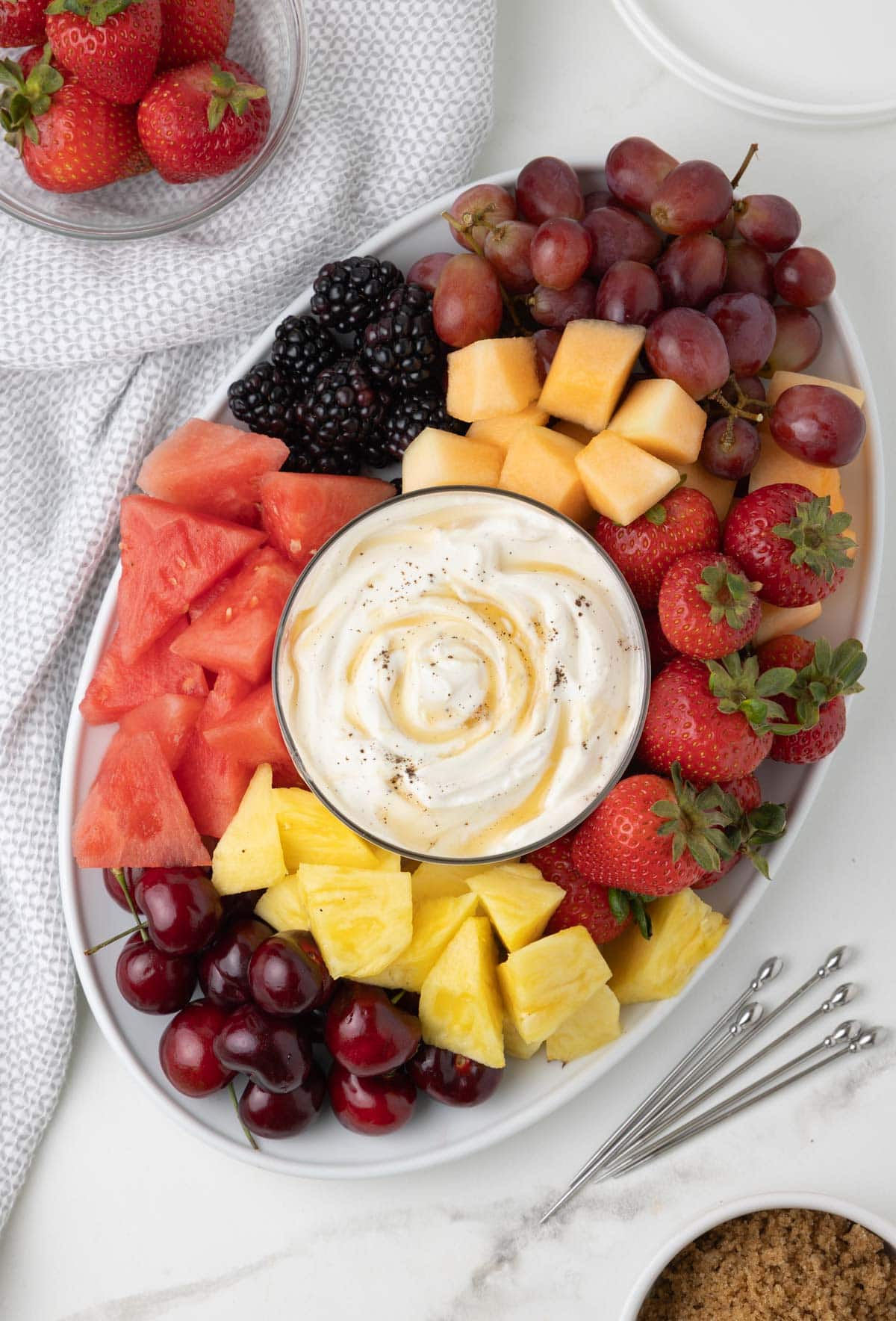 A platter of colorful fresh fruit, strawberries, cherries, pineapple, grapes, melon, and a honey topped fruit rip.