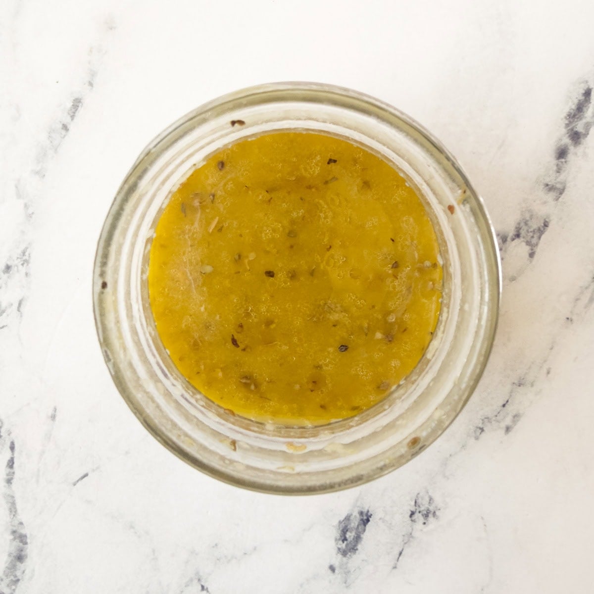 A jar of Greek vinaigrette dressing shaken to combine.