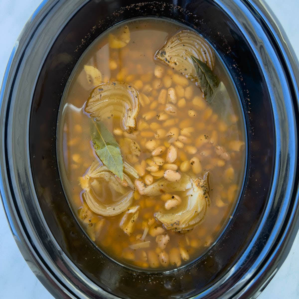 Finished crock pot pinto beans, with hunks of cooked onions and bay leaves.