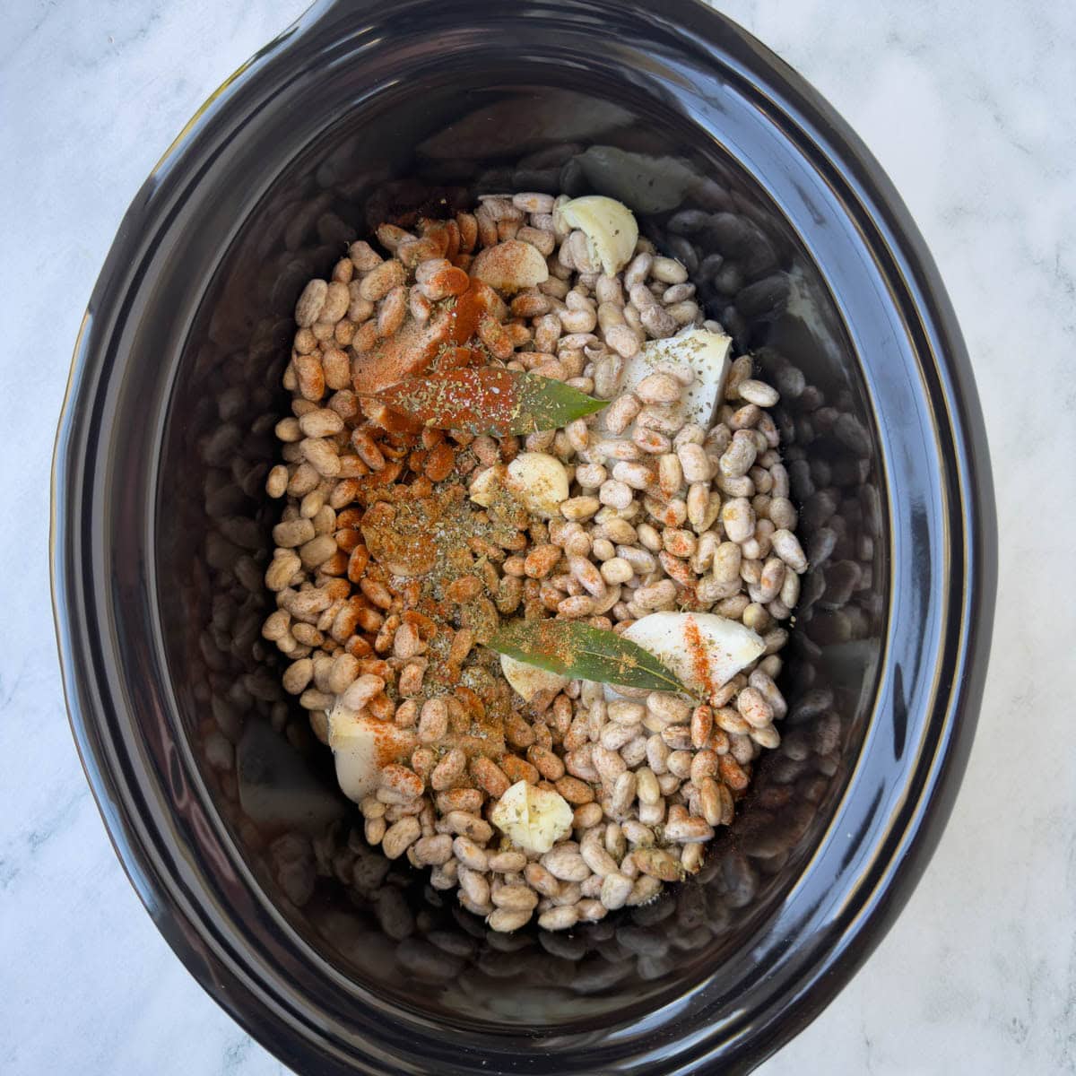 Pinto beans and spices in a slow cooker crock ready for slow cooking.