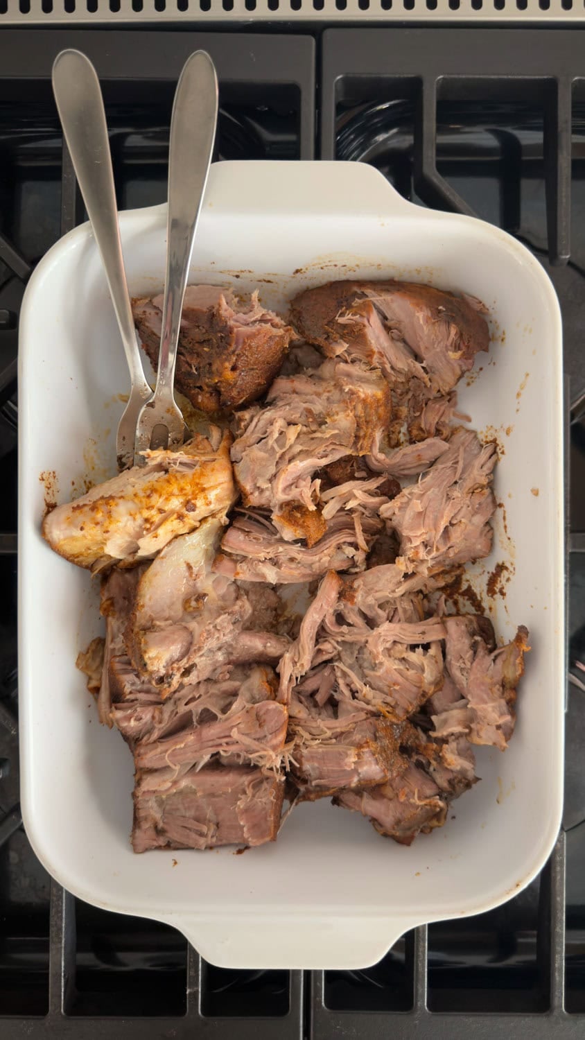 Large hunks of pork shoulder in a casserole dish with two large forks for pulling.