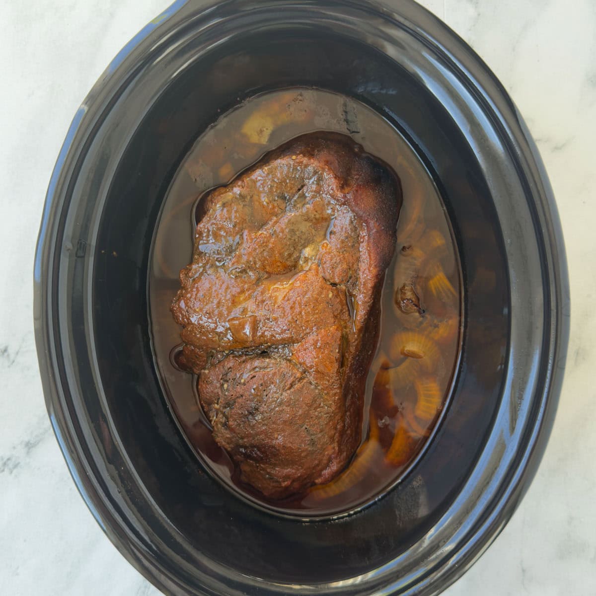 A finished slow cooker pork butt ready for draining and shredding.