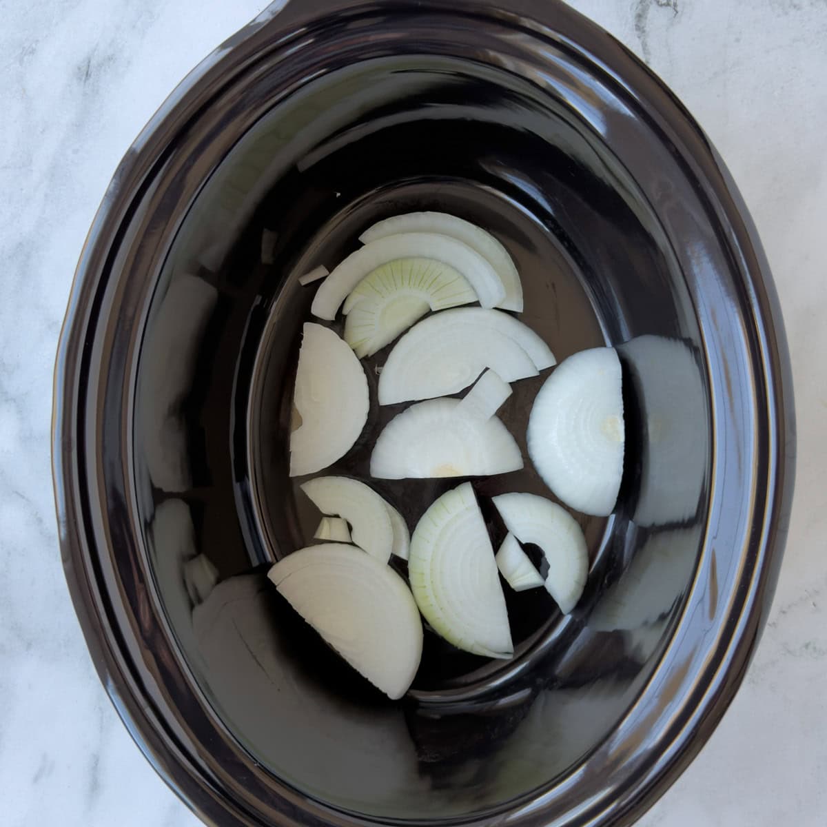 White onion chunks in the bottom of a slow cooker crock.