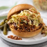 A slow cooker pulled pork sandwich with coleslaw and pickles.