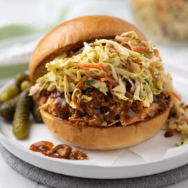 A slow cooker pulled pork sandwich with coleslaw and pickles.