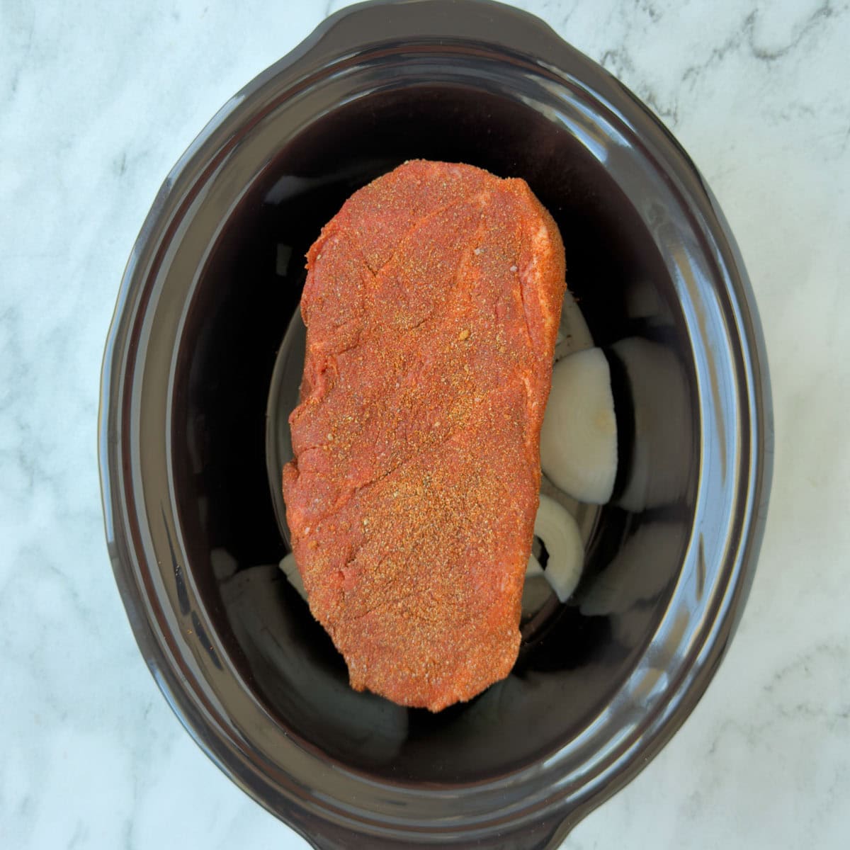 A pork shoulder seasoned and ready for slow cooking in a black dish.