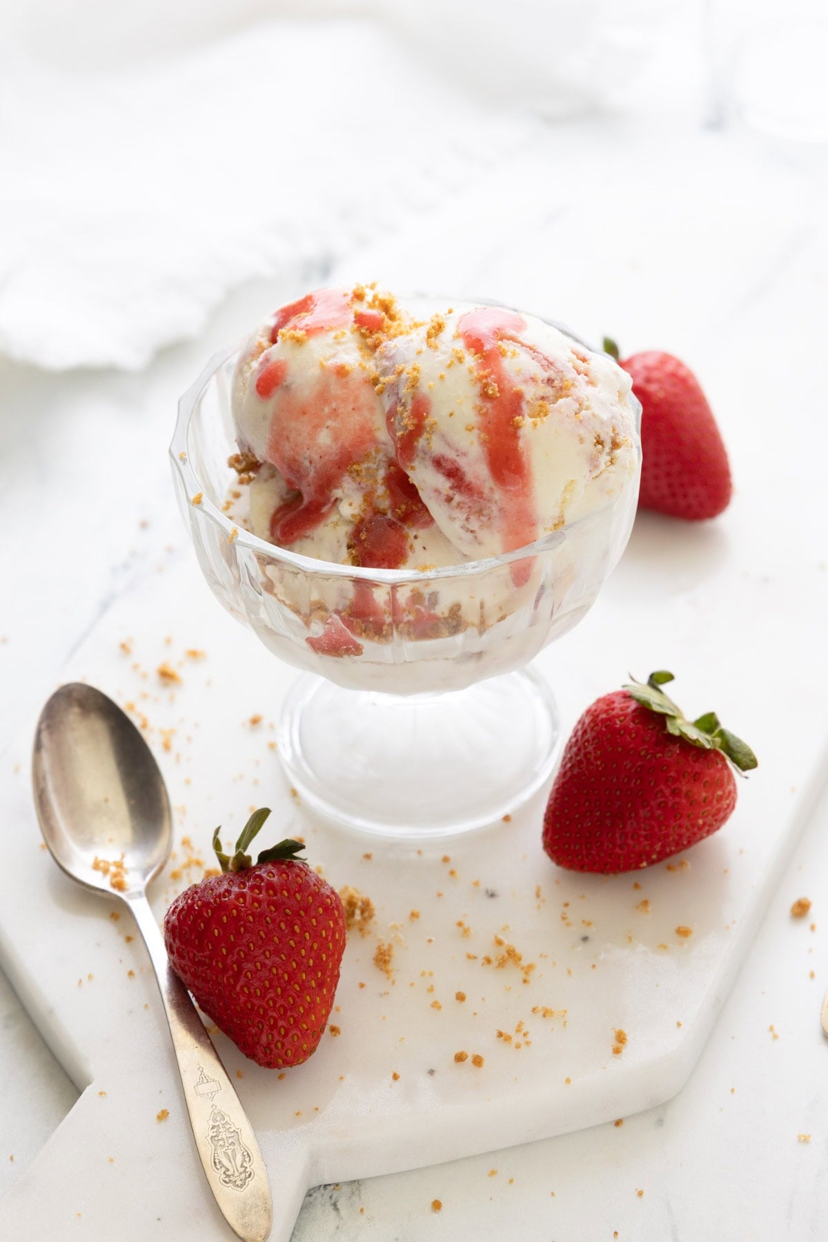 A bowl of strawberry cheesecake ice cream with graham sprinkles and strawberry sauce.
