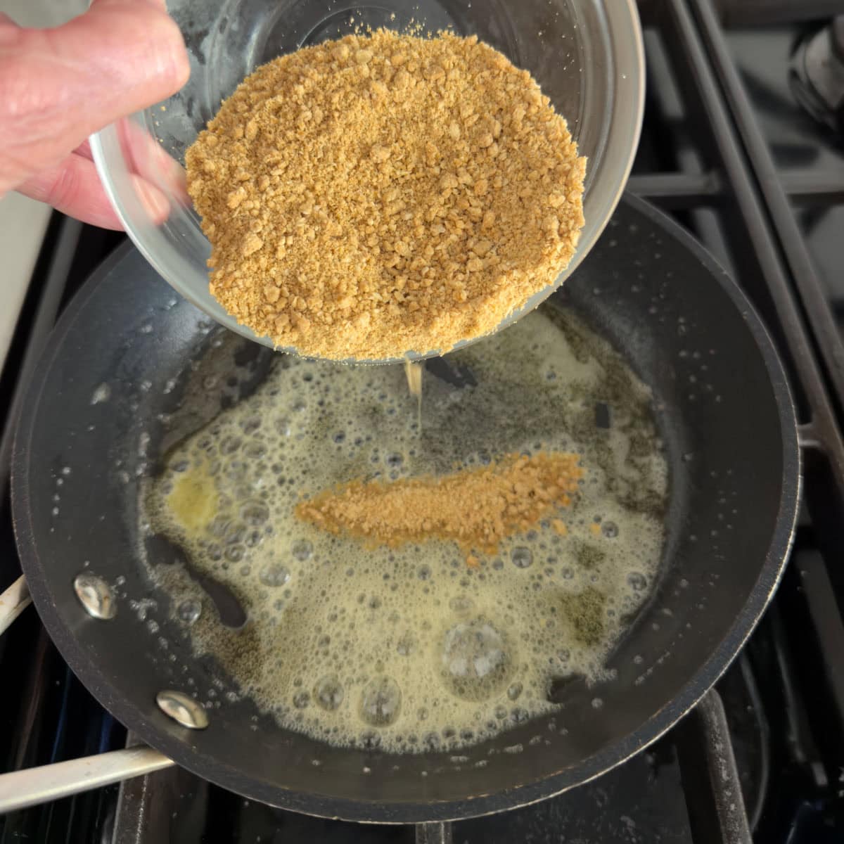 Adding golden graham crackers crumbs to a small pan with melted butter to toast.