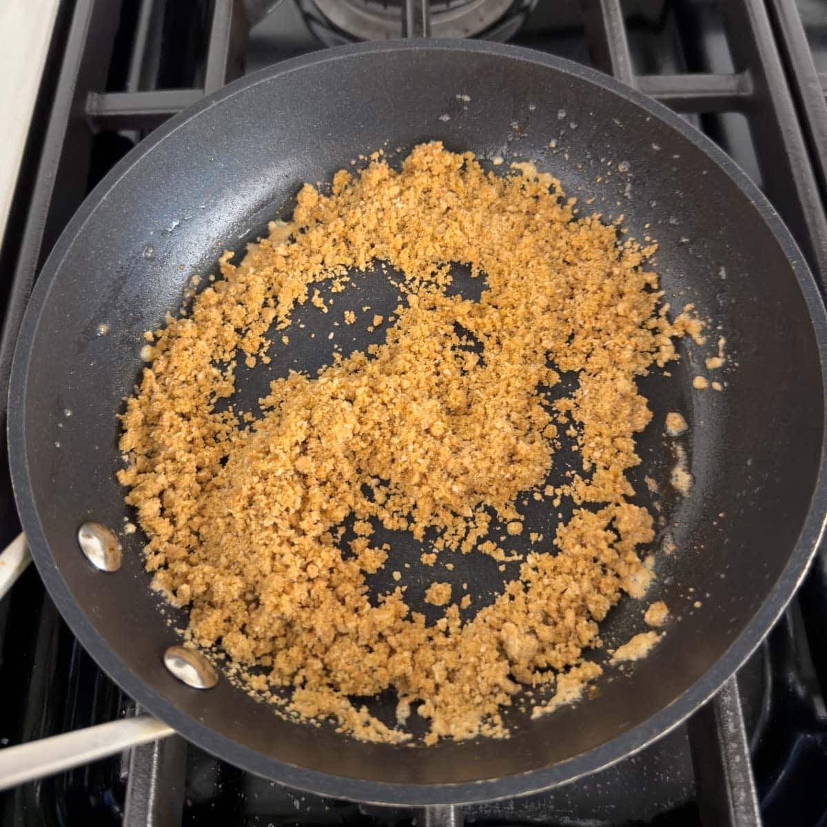 Buttered graham crumbs in a small pan to use as a crumble for strawberry cheesecake ice cream.