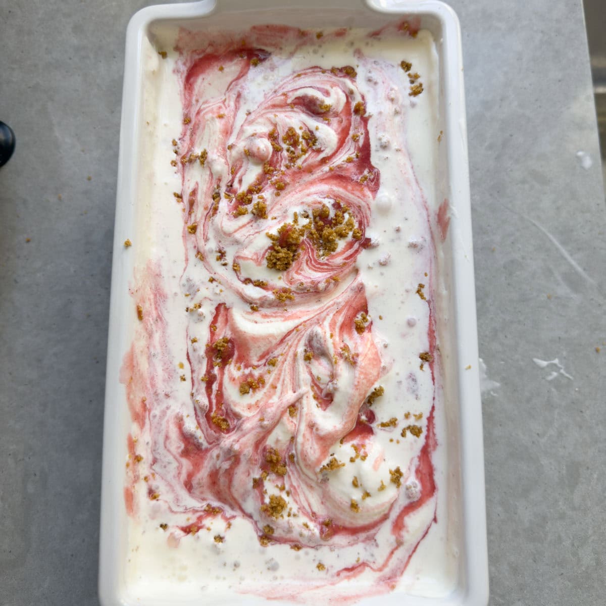 Finished cheesecake ice cream smoothed into a white ceramic loaf pan with swirls of strawberry.