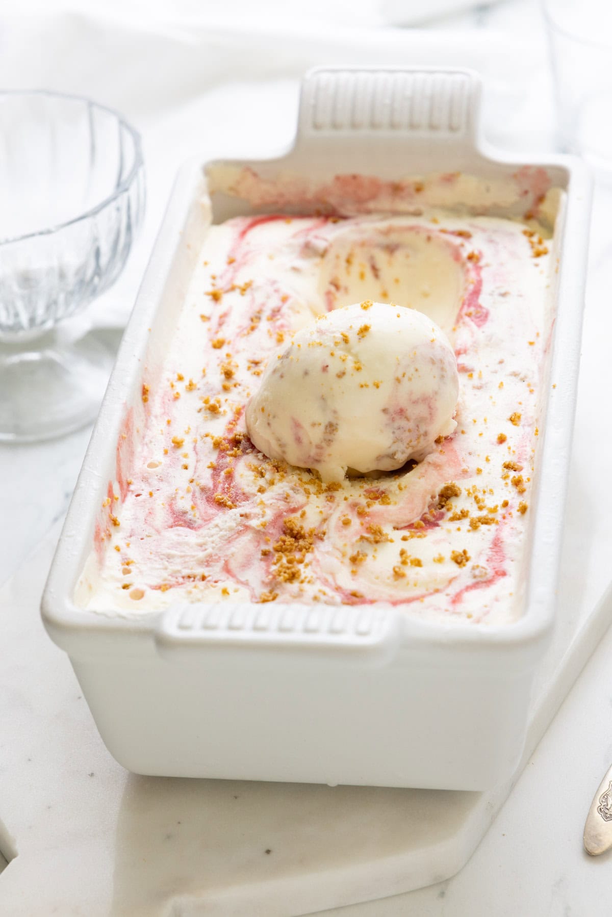 A white loaf pan of strawberry cheesecake ice cream with a scoop sitting on top.