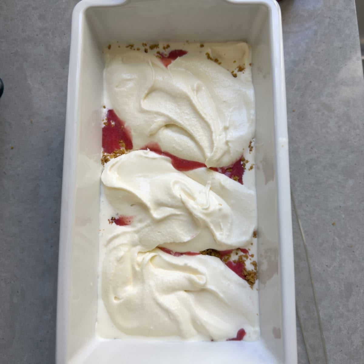 Second layer of strawberry cheesecake ice cream creating swirls in a loaf pan.