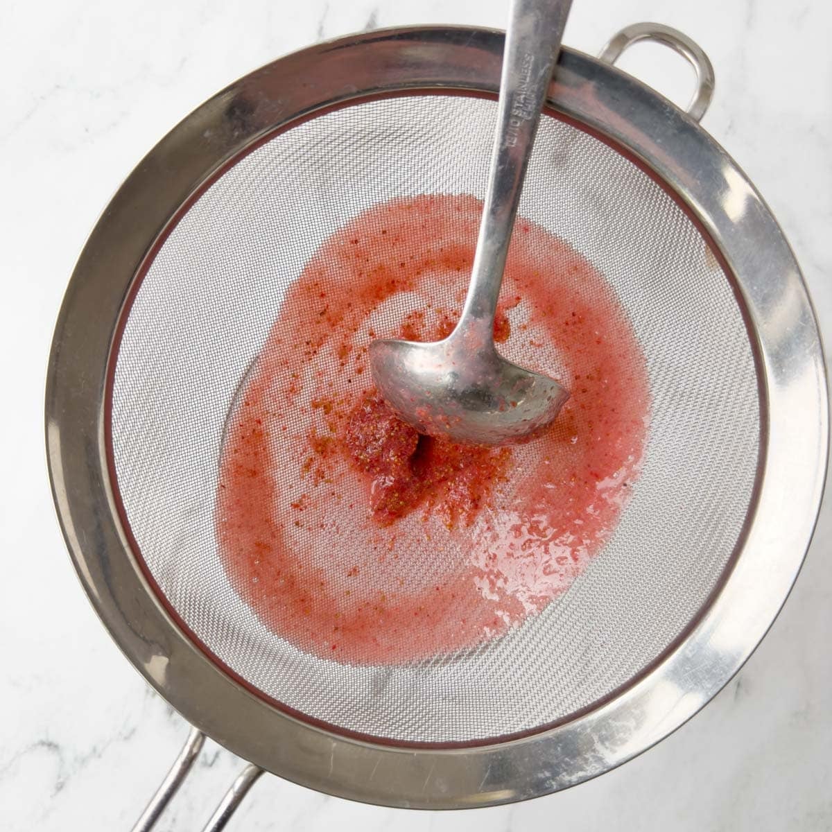 Seeding a strawberry sauce through a sieve with a ladel.