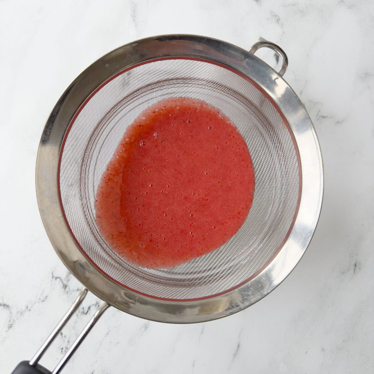 Pureed strawberries in a fine sieve over a bowl.