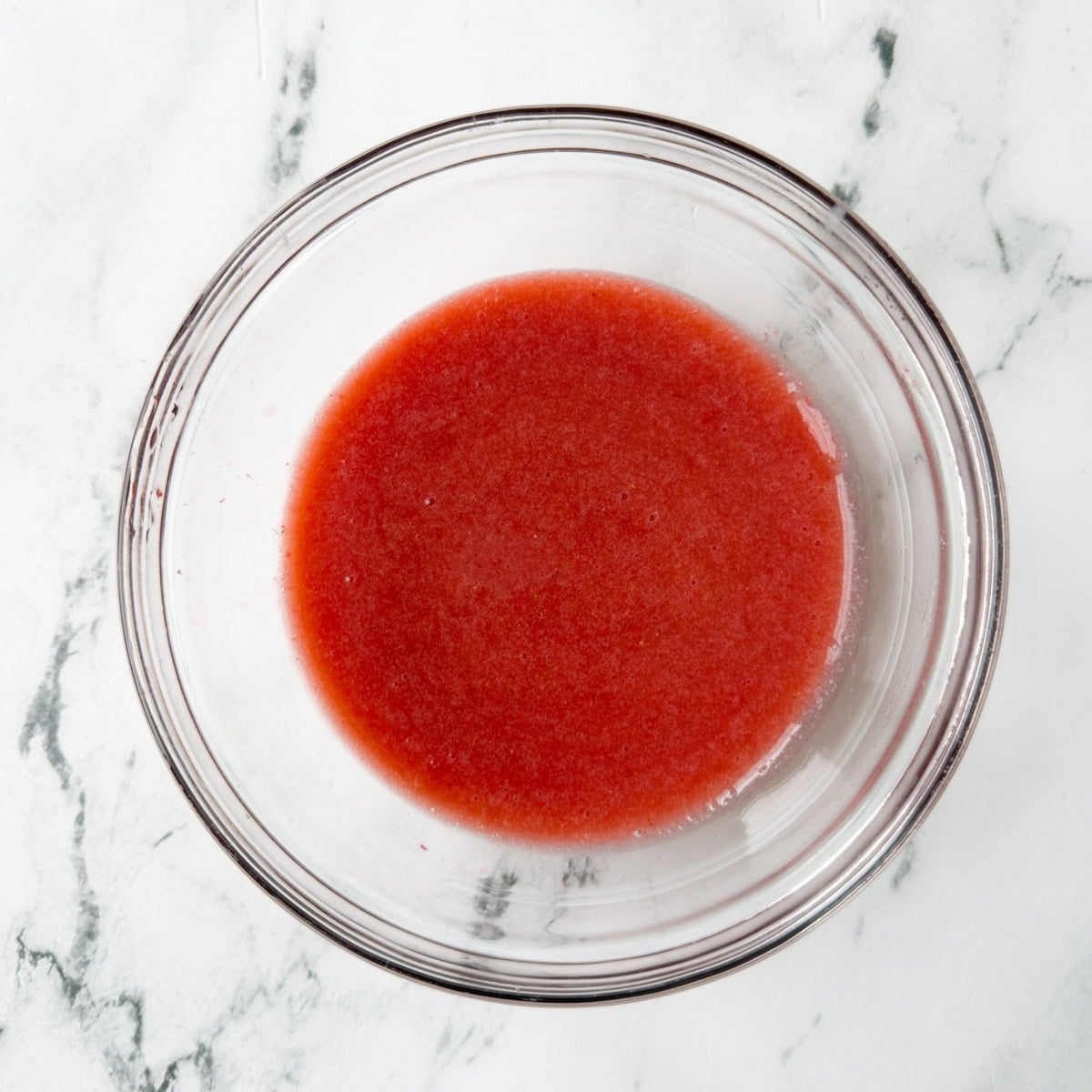 Finished bright red strawberry sauce in a glass bowl.