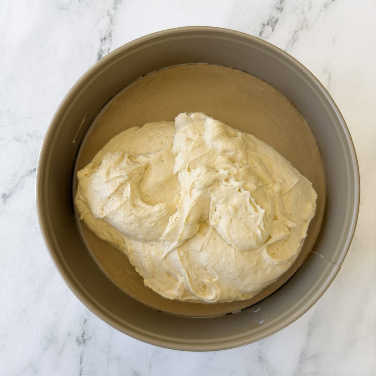 Mixed cake batter in a springform pan lined with parchment paper.
