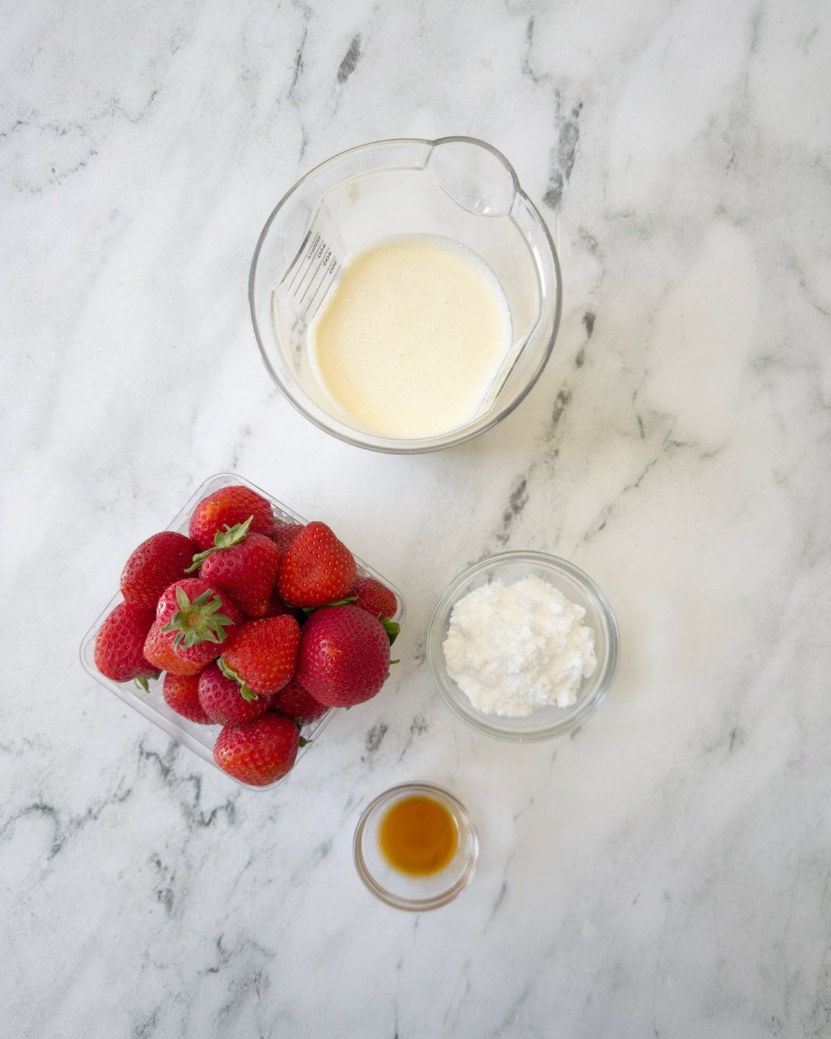 Heavy whipping cream, fresh red strawberries, vanilla extract and sugar in bowls for cake topping.