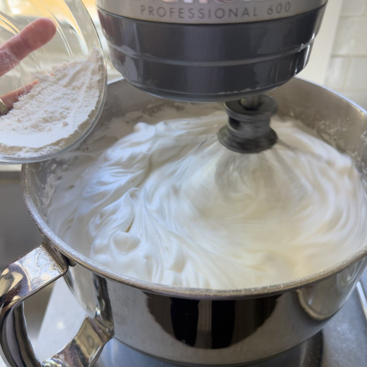Adding sugar to whipped eggs white for angel food cake batter in a workbowl.