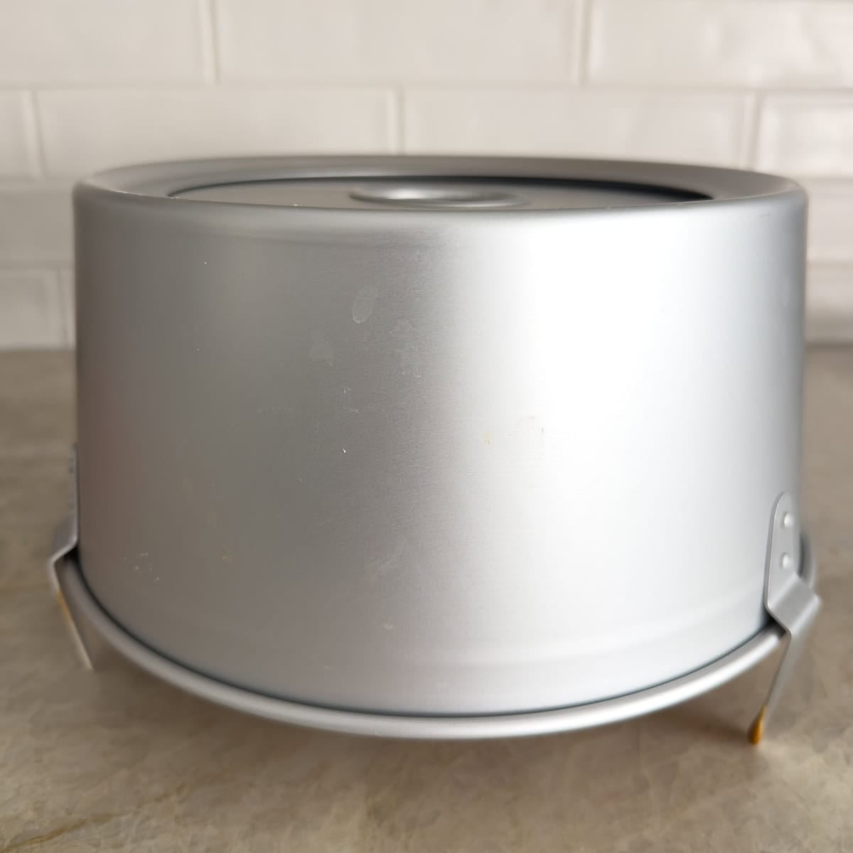 An angel food cake inverted on the counter, cooling, in a silver tube pan.