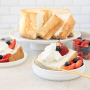 A slice of angel food cake on a plate with whipped cream, strawberries, and blueberries.