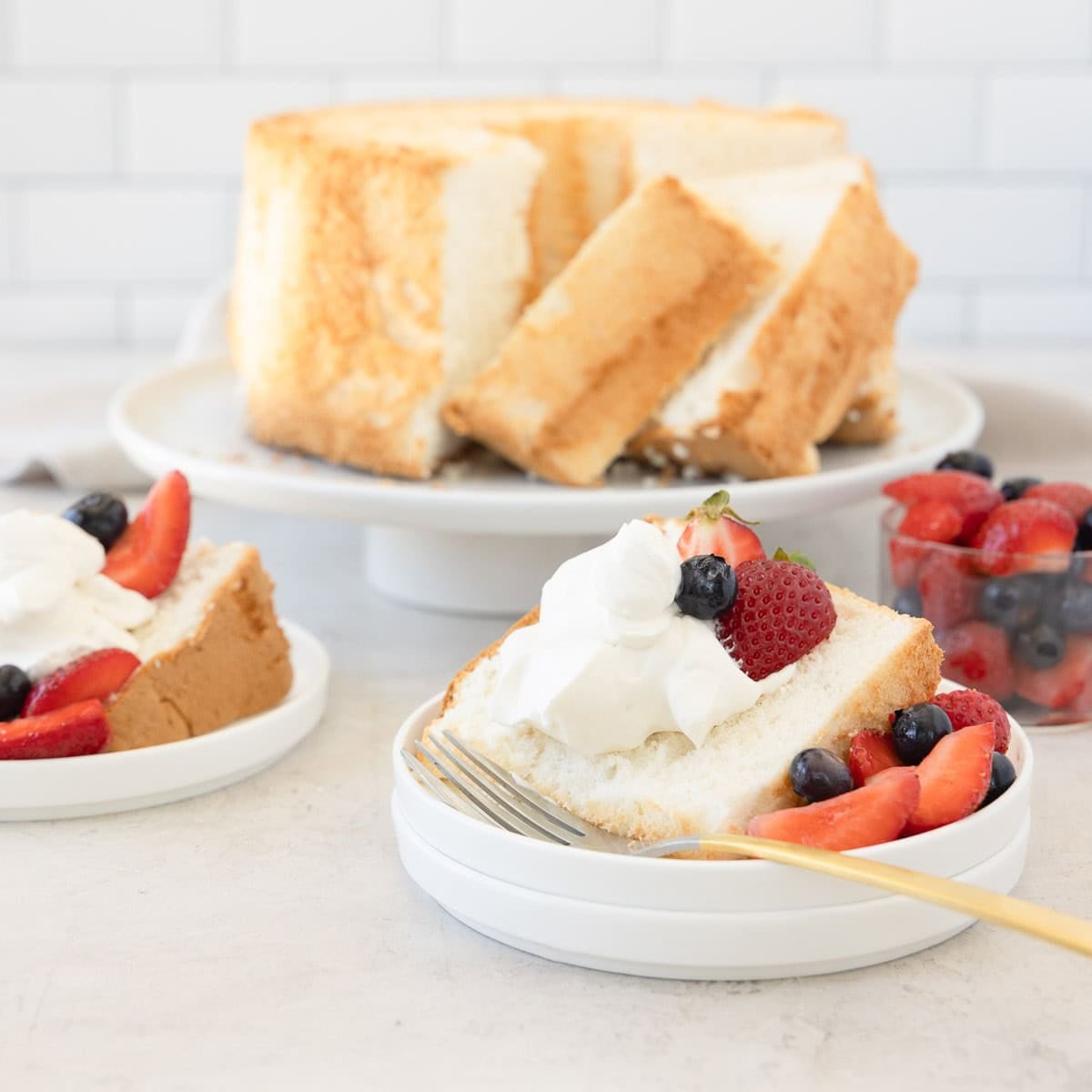 A slice of angel food cake on a plate with whipped cream, strawberries, and blueberries.