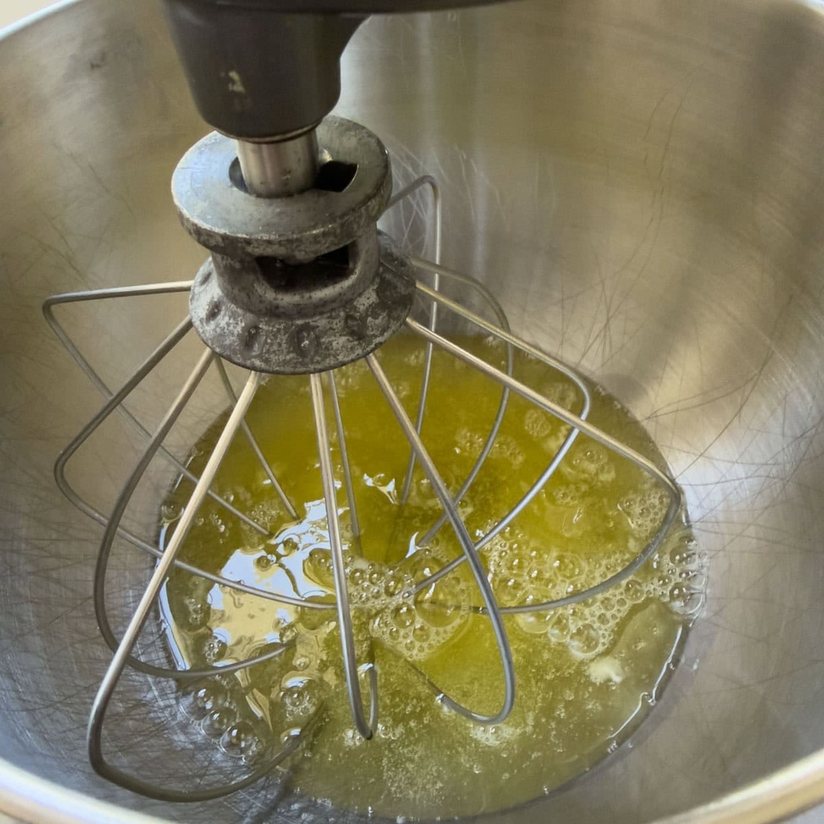 A dozen eggs whites in a stainless steel mixing bowl with whisk attachment.