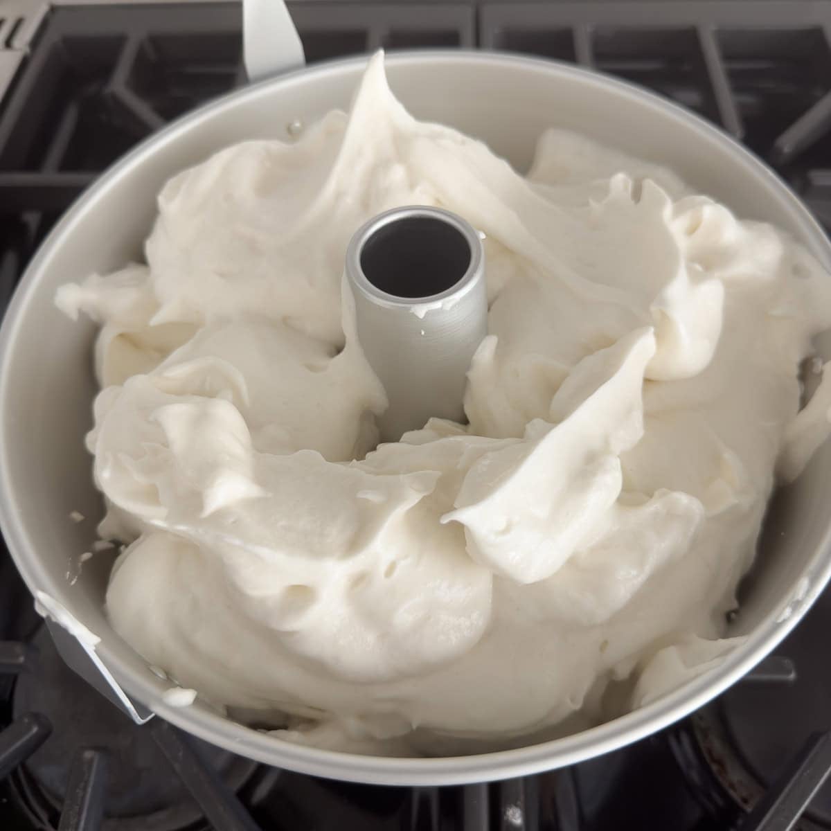 Spooning meringue cake batter into a silver tube cake pan.