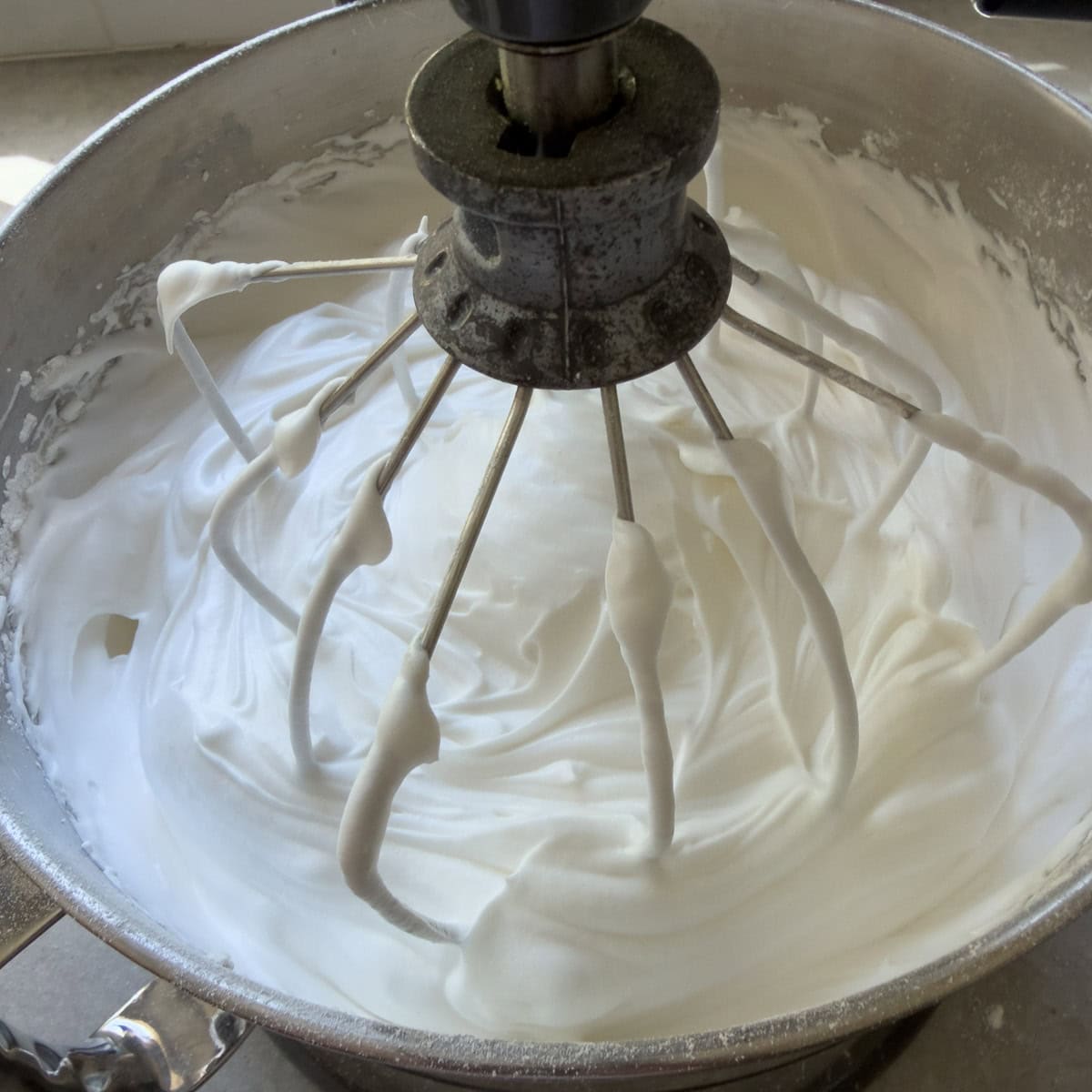 White angel food cake batter with a stainless steel wire whip attachment in a mixing bowl.