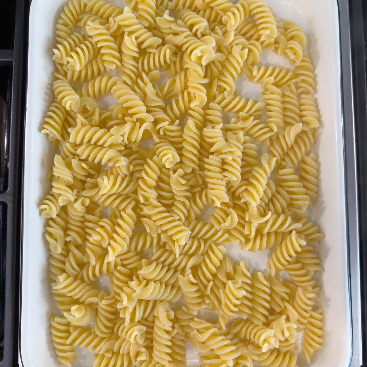 Cooked corkscrew pasta cooling on a sheet tray for making pasta salad.